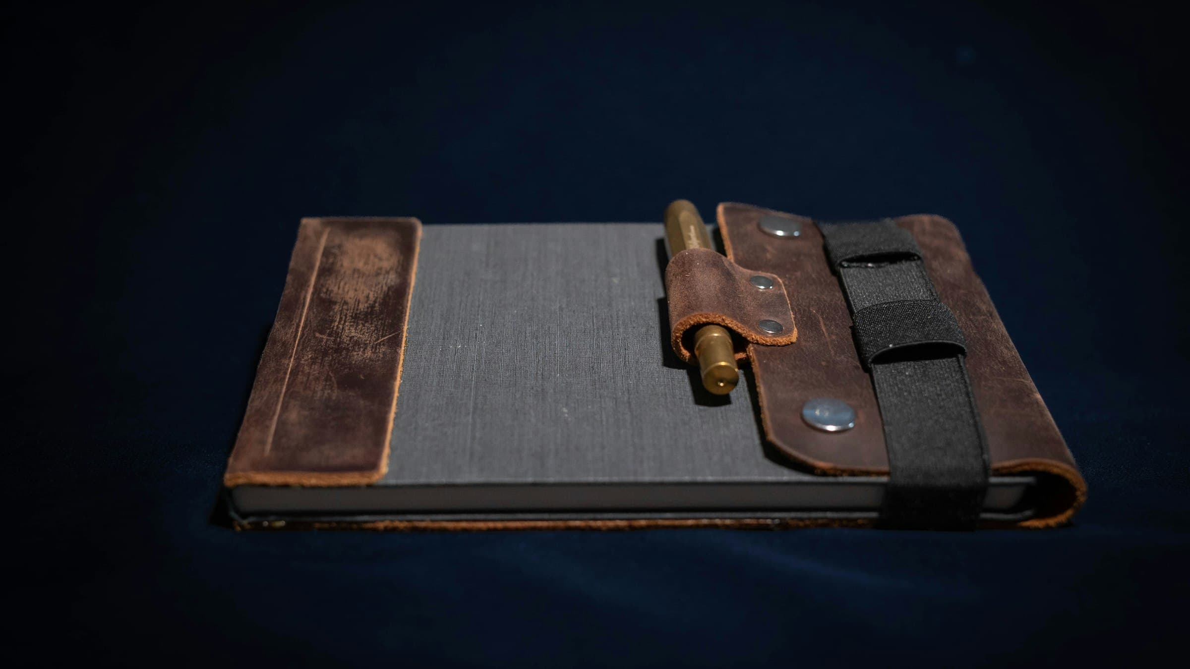 A closed leather notebook with a pen on a dark background