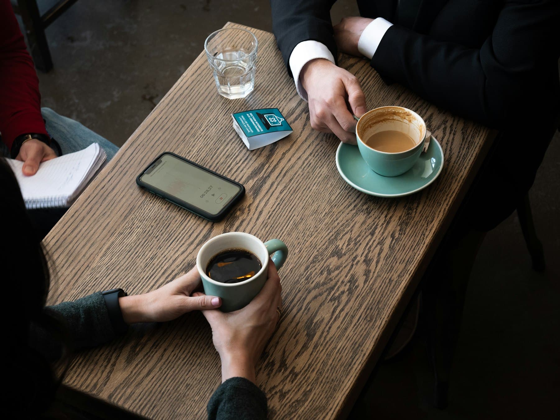 Two people talking at a wooden table, with coffee and a notebook