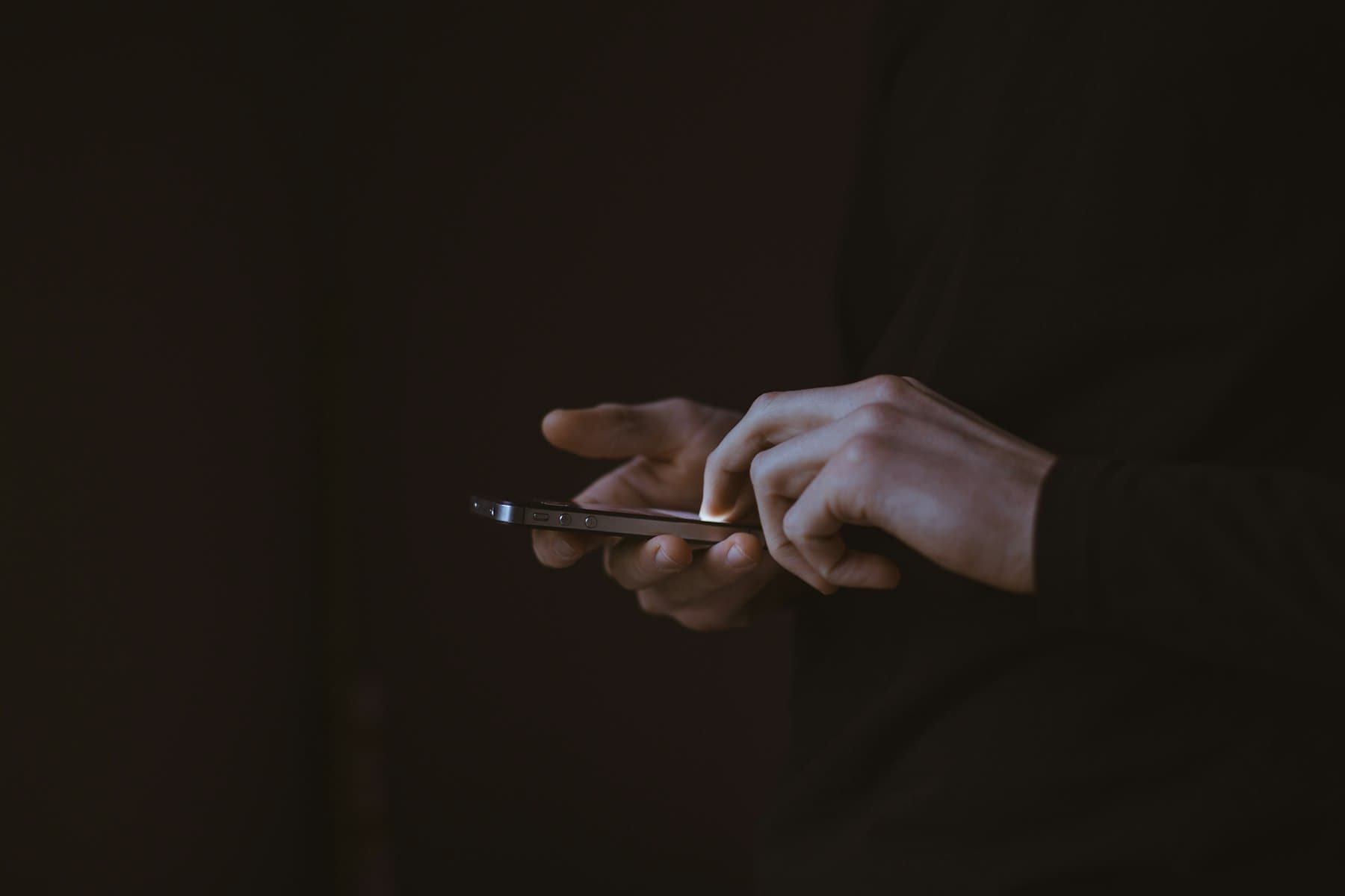 Hands holding a glowing smartphone in a dark room