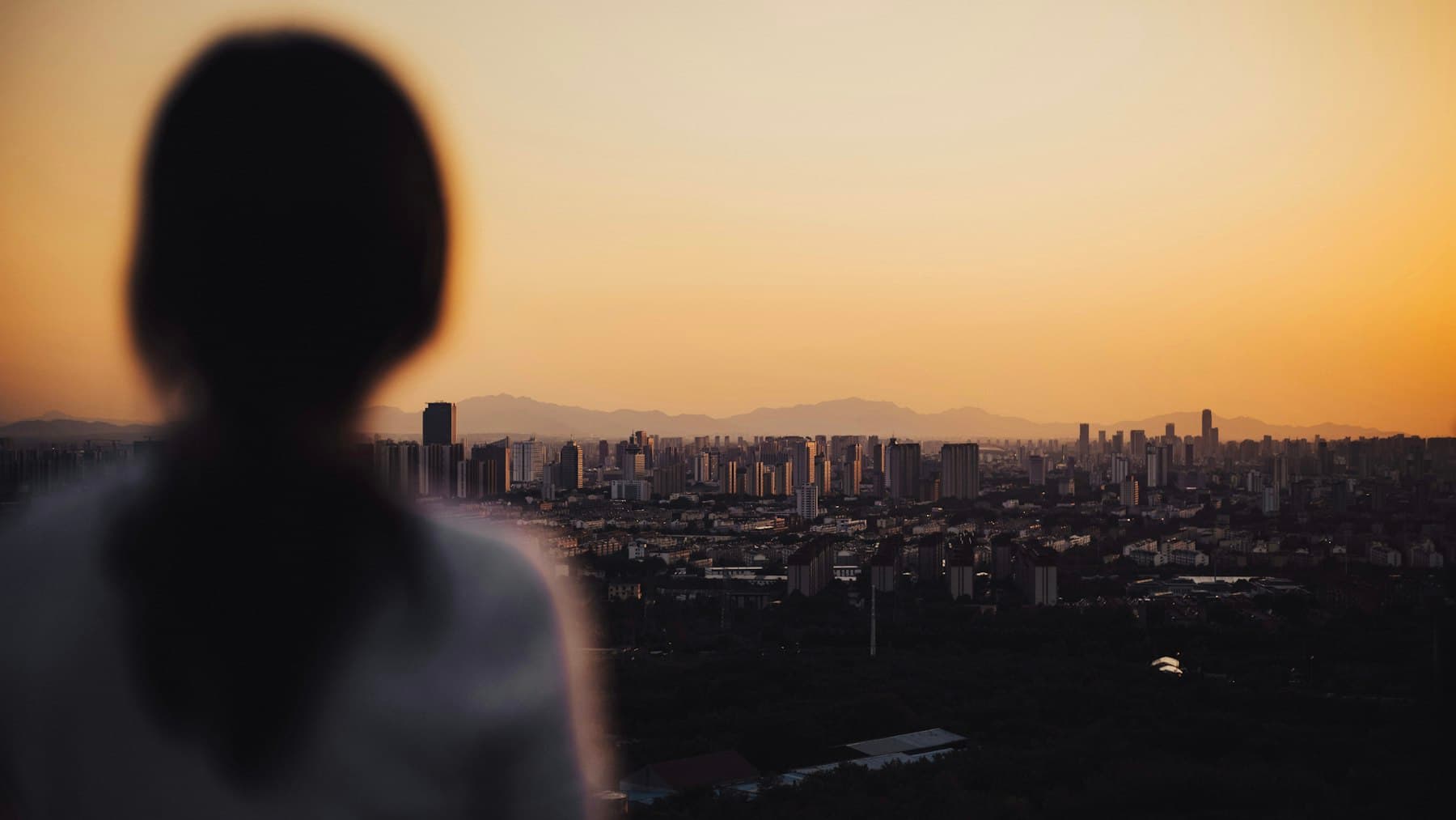 Een vrouw, van achteren gezien, kijkt bij zonsondergang uit over de stad