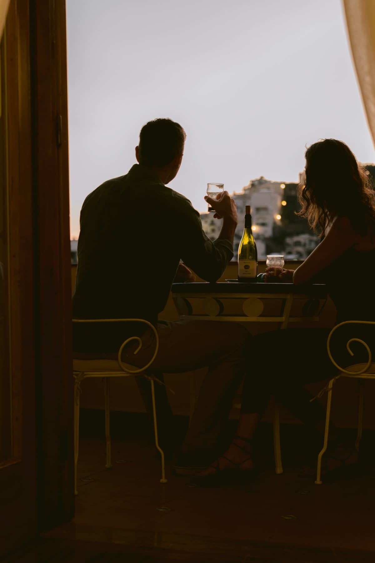 Een stel, van achteren gezien, met een glas wijn op een balkon bij schemering