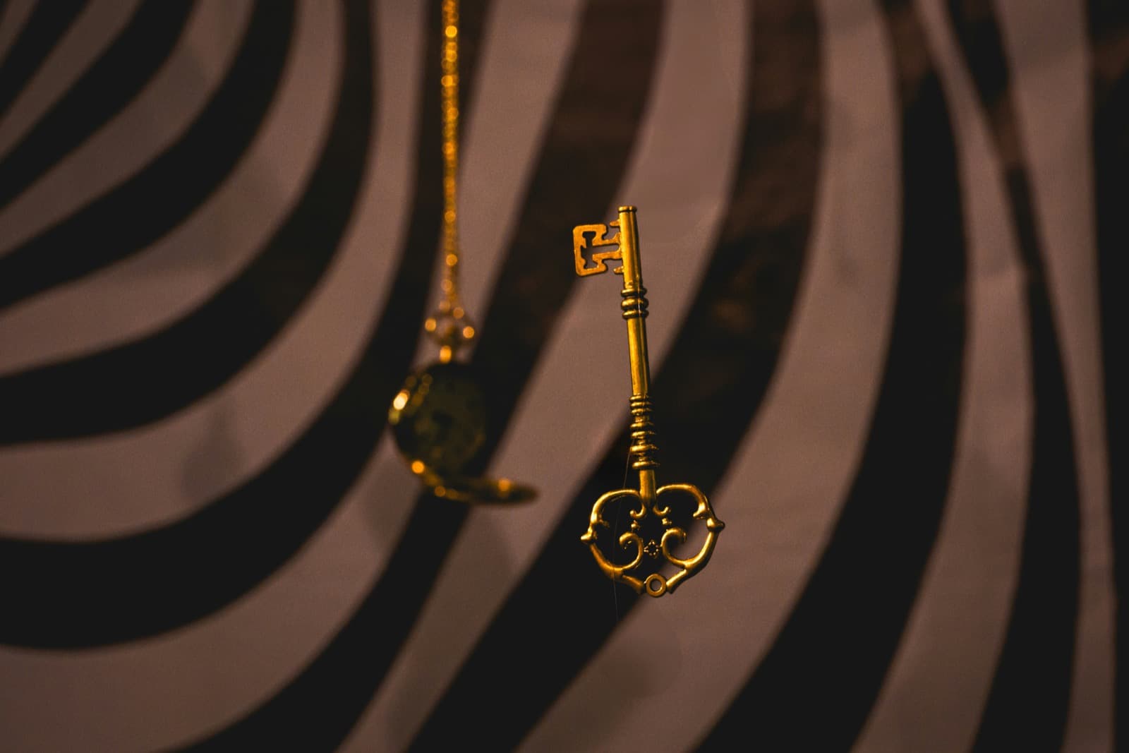 Een gouden sleutel met een hartvormige kop hangt aan een fijne ketting, tegen een donkere, wervelende achtergrond