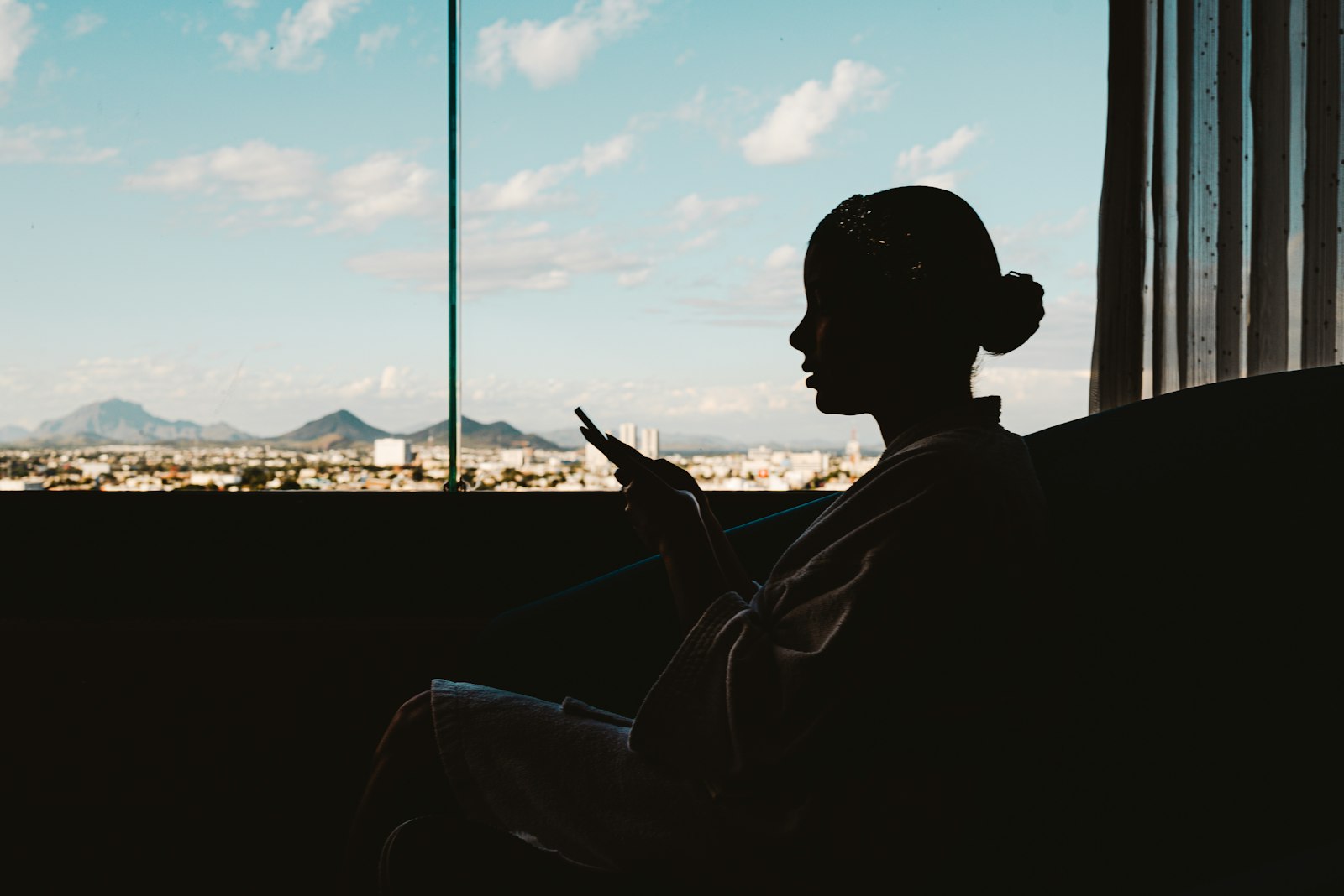 Silhouet van een vrouw met haar telefoon bij een raam met uitzicht over de stad