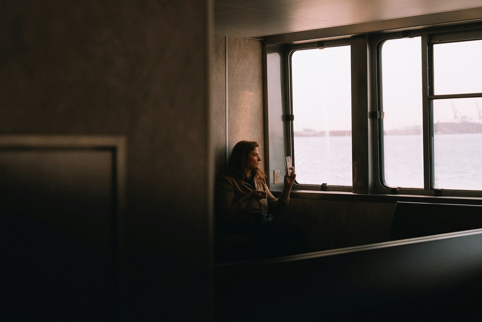 Een vrouw kijkt rustig op haar telefoon bij het raam van een veerboot
